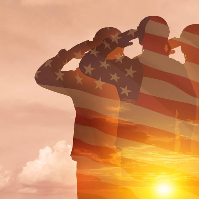 Three silhouetted soldiers salute, overlaid with a transparent American flag, with a bright sun setting in the background.